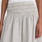 Close-up of a smocked high-waisted skirt with vertical pinstripes in beige and white, worn by a model.