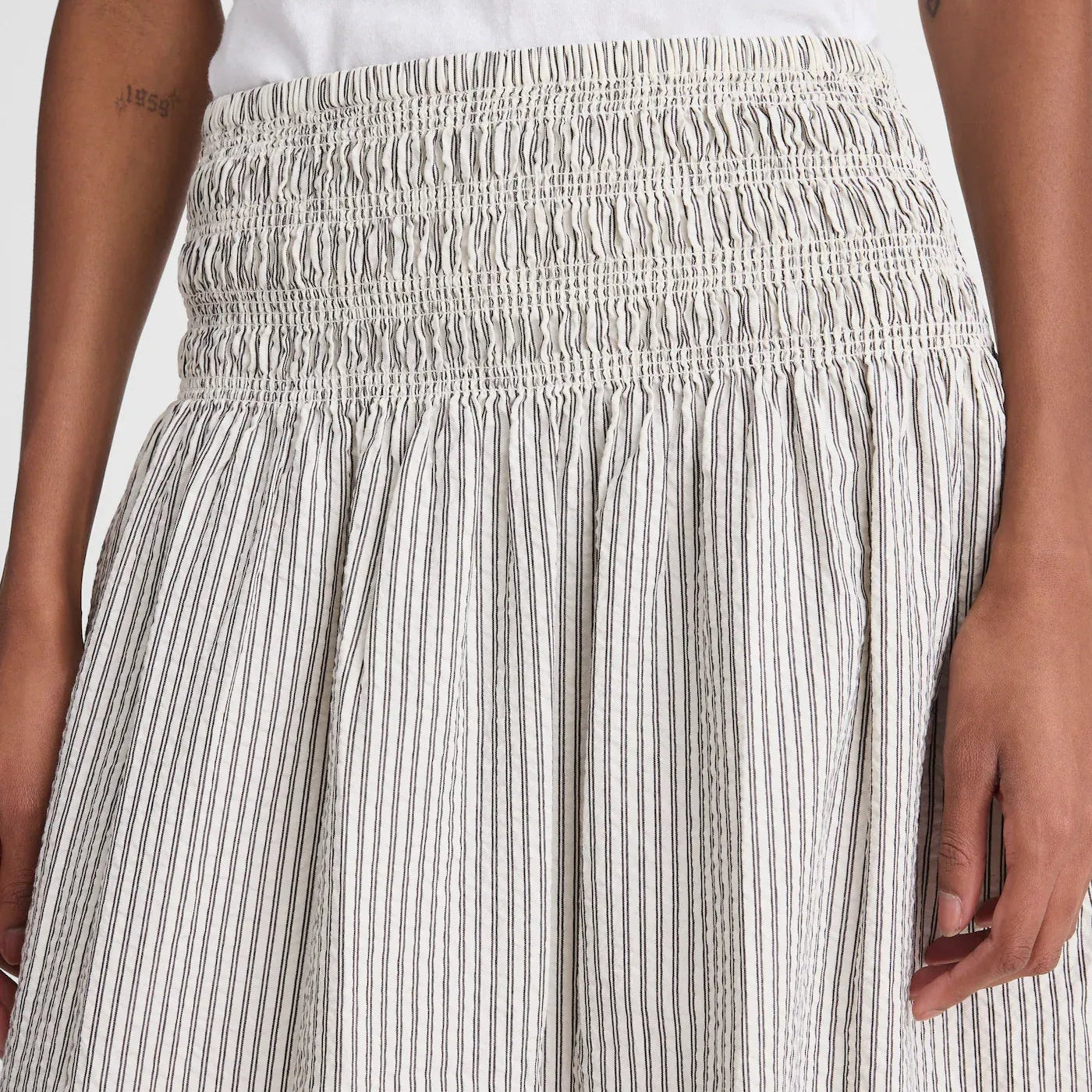 Close-up of a smocked high-waisted skirt with vertical pinstripes in beige and white, worn by a model.