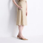 A woman models a beige sleeveless midi dress with a matching cropped top, standing against a plain white wall.