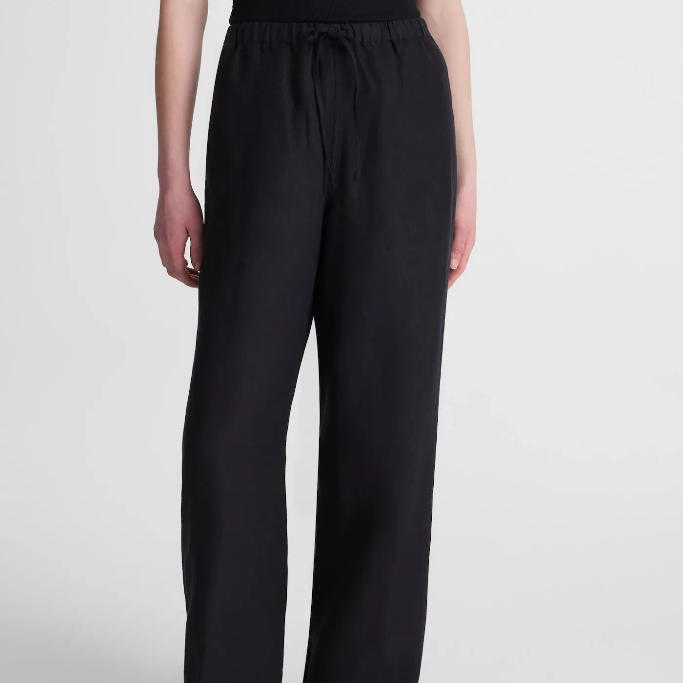A model wearing black wide-leg drawstring pants and black sandals, shown from the waist down against a light gray studio background.