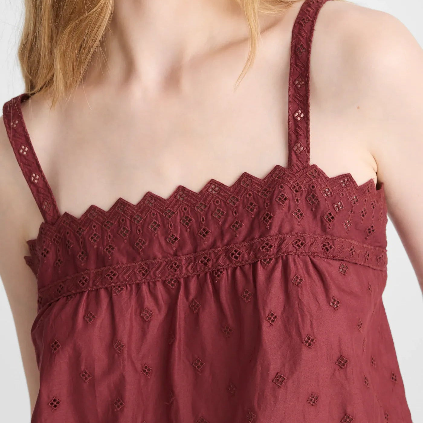 Close-up of a woman wearing a burgundy eyelet lace camisole top with thin straps and a scalloped neckline.