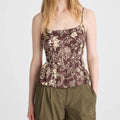 A woman modeling a brown floral camisole top with thin straps and olive green pants against a light gray studio background.