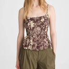 A woman modeling a brown floral camisole top with thin straps and olive green pants against a light gray studio background.