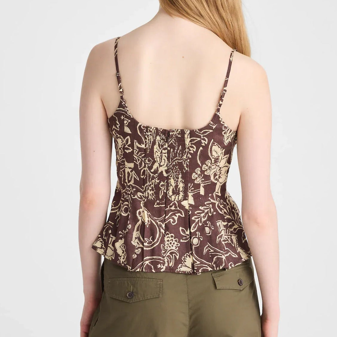 A woman shown from the back wearing a brown and beige patterned spaghetti-strap top and olive green pants, against a light gray studio background.