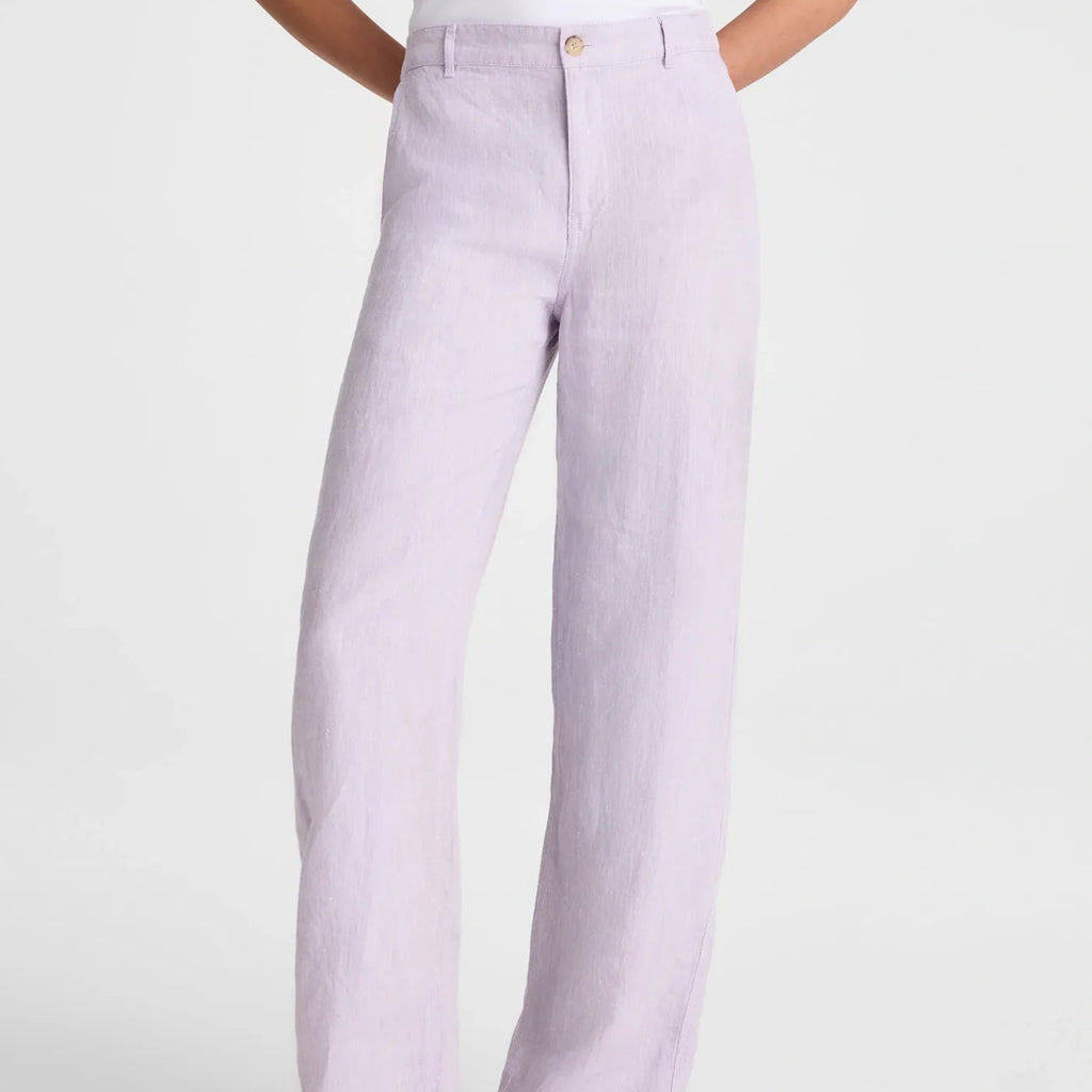 A person wearing light lavender wide-leg linen pants with a white top and black flip-flop sandals, shown from the waist down against a light gray studio background.