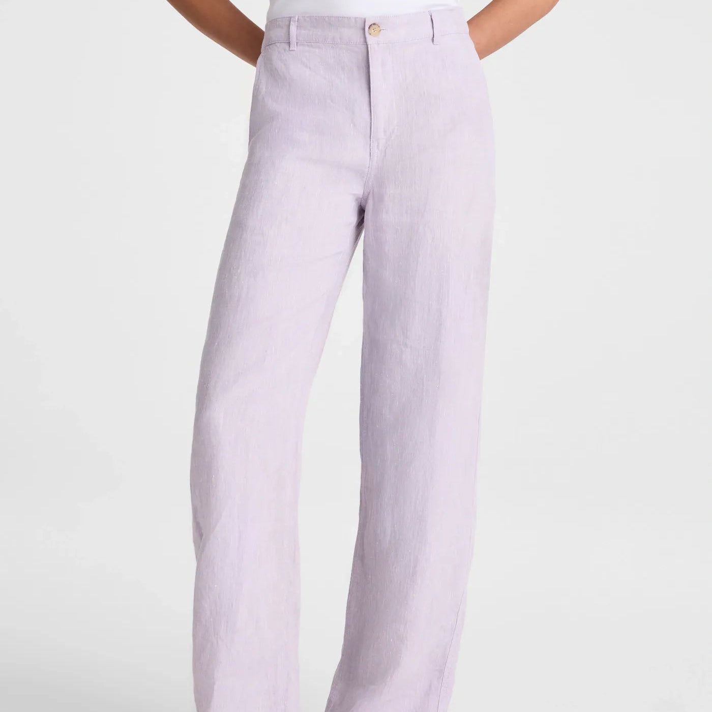 A person wearing light lavender wide-leg linen pants with a white top and black flip-flop sandals, shown from the waist down against a light gray studio background.