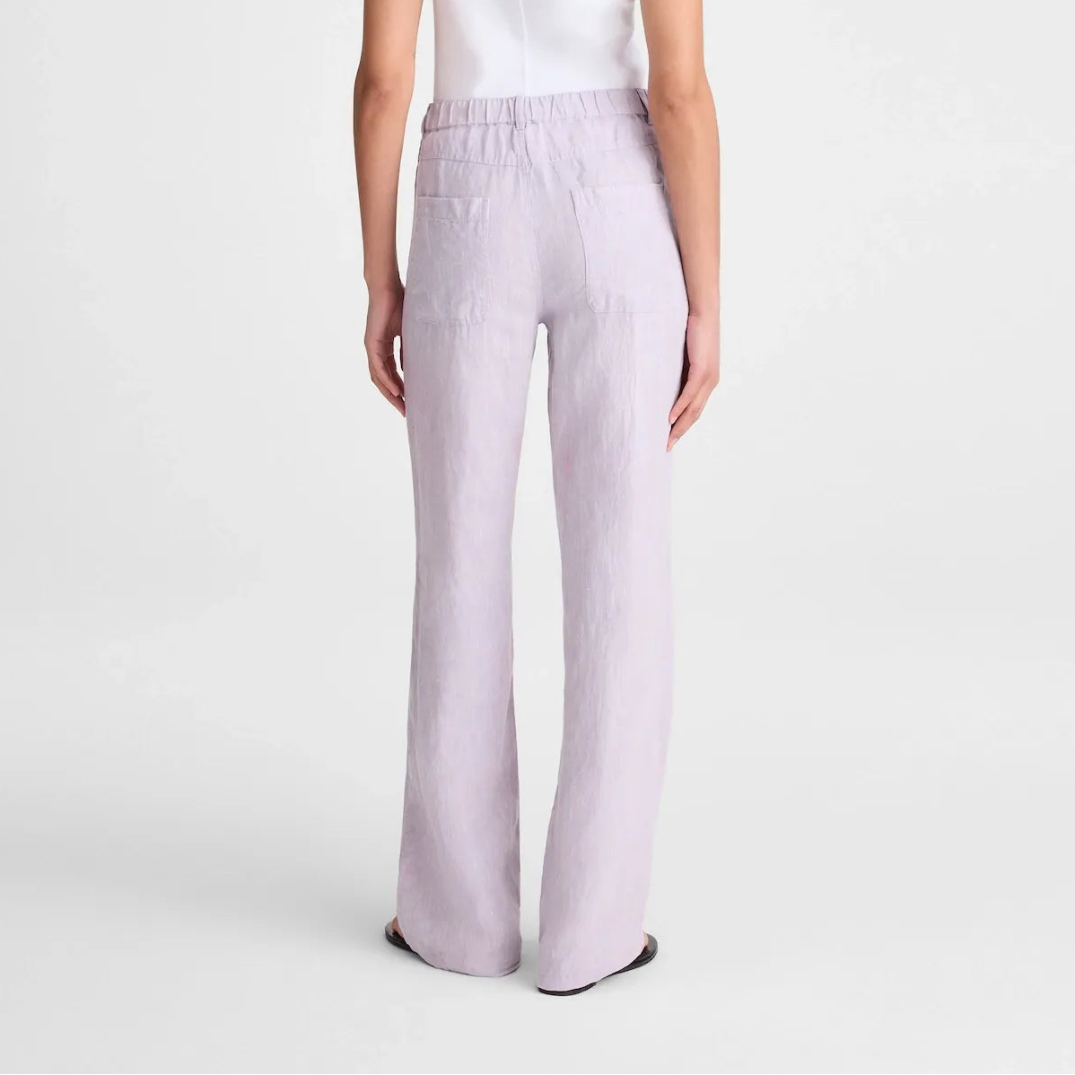 A model shown from the back wearing a sleeveless white top and light lavender wide-leg trousers against a plain light gray studio background.