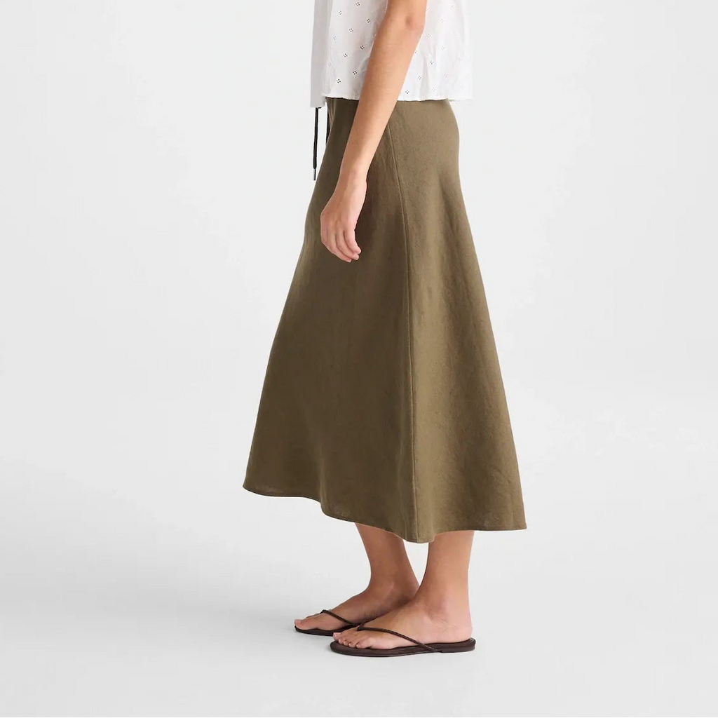 A woman modeling a white sleeveless lace-trim camisole and an olive green midi skirt, standing against a plain light gray studio background.