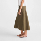 A woman modeling a white sleeveless lace-trim camisole and an olive green midi skirt, standing against a plain light gray studio background.