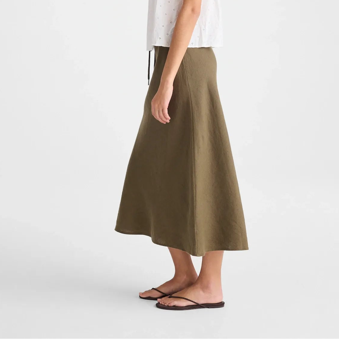 A woman modeling a white sleeveless lace-trim camisole and an olive green midi skirt, standing against a plain light gray studio background.