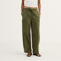 A model stands against a plain light background wearing olive green wide-leg drawstring pants, a white short-sleeve cropped T-shirt, and dark sandals.