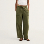 A model stands against a plain light background wearing olive green wide-leg drawstring pants, a white short-sleeve cropped T-shirt, and dark sandals.
