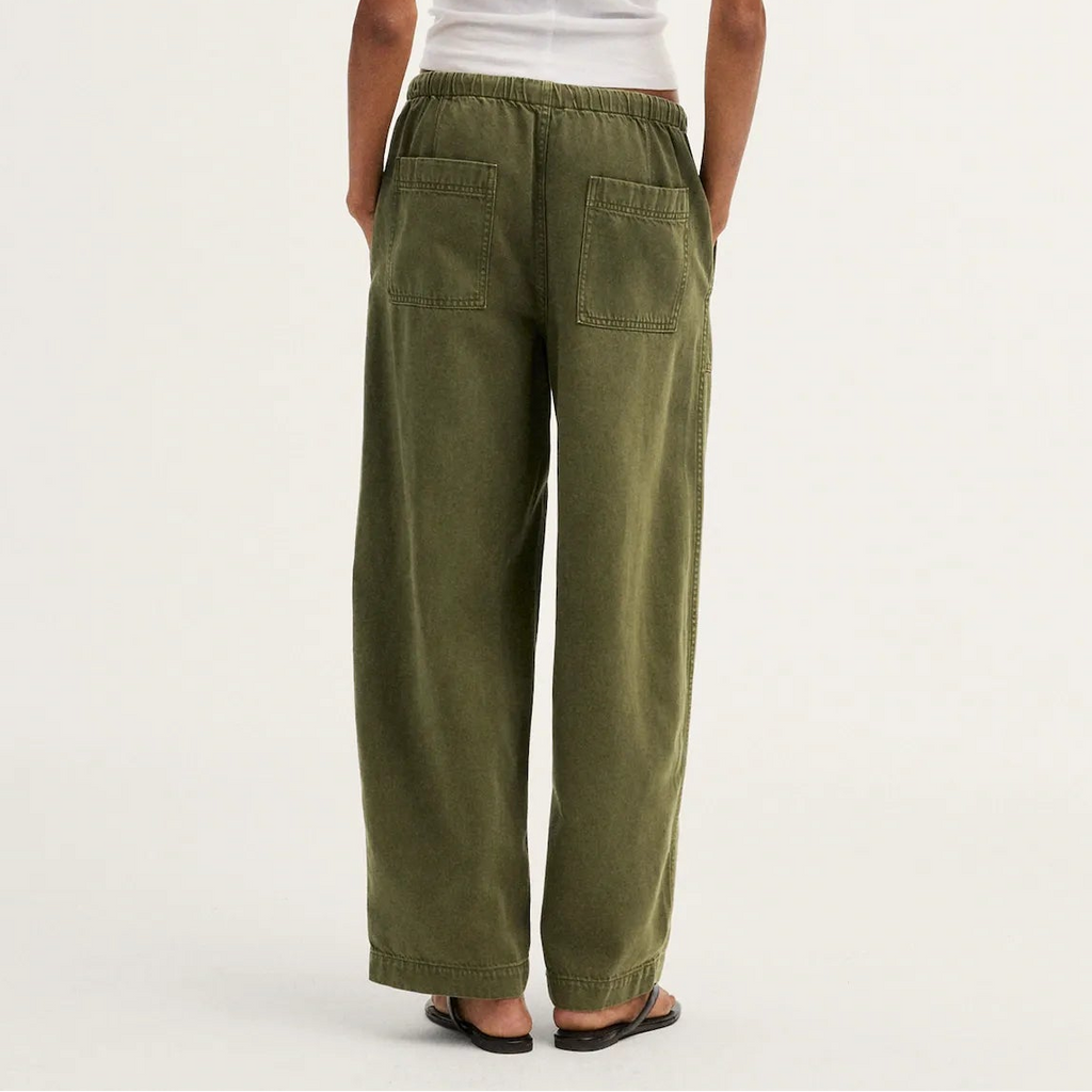 A model shown from the back wearing olive green wide-leg pants, a white short-sleeve t-shirt, and black sandals against a plain off-white studio background.