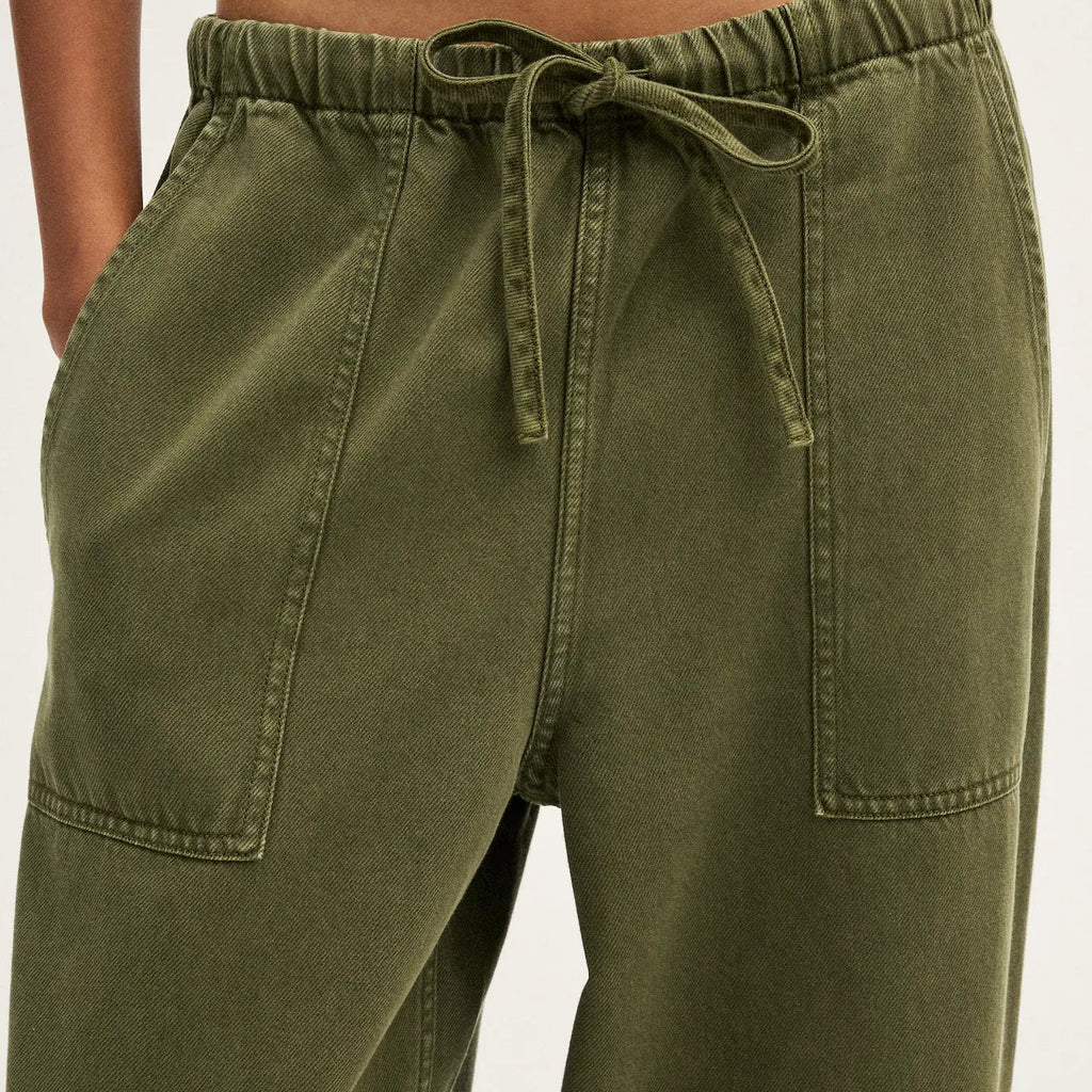 Close-up of a person wearing olive green drawstring pants with side pockets, paired with a white cropped top against a light neutral background.