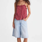 A woman modeling a red and white polka dot spaghetti strap top paired with light-wash denim culottes and brown sandals, standing against a plain white studio background.