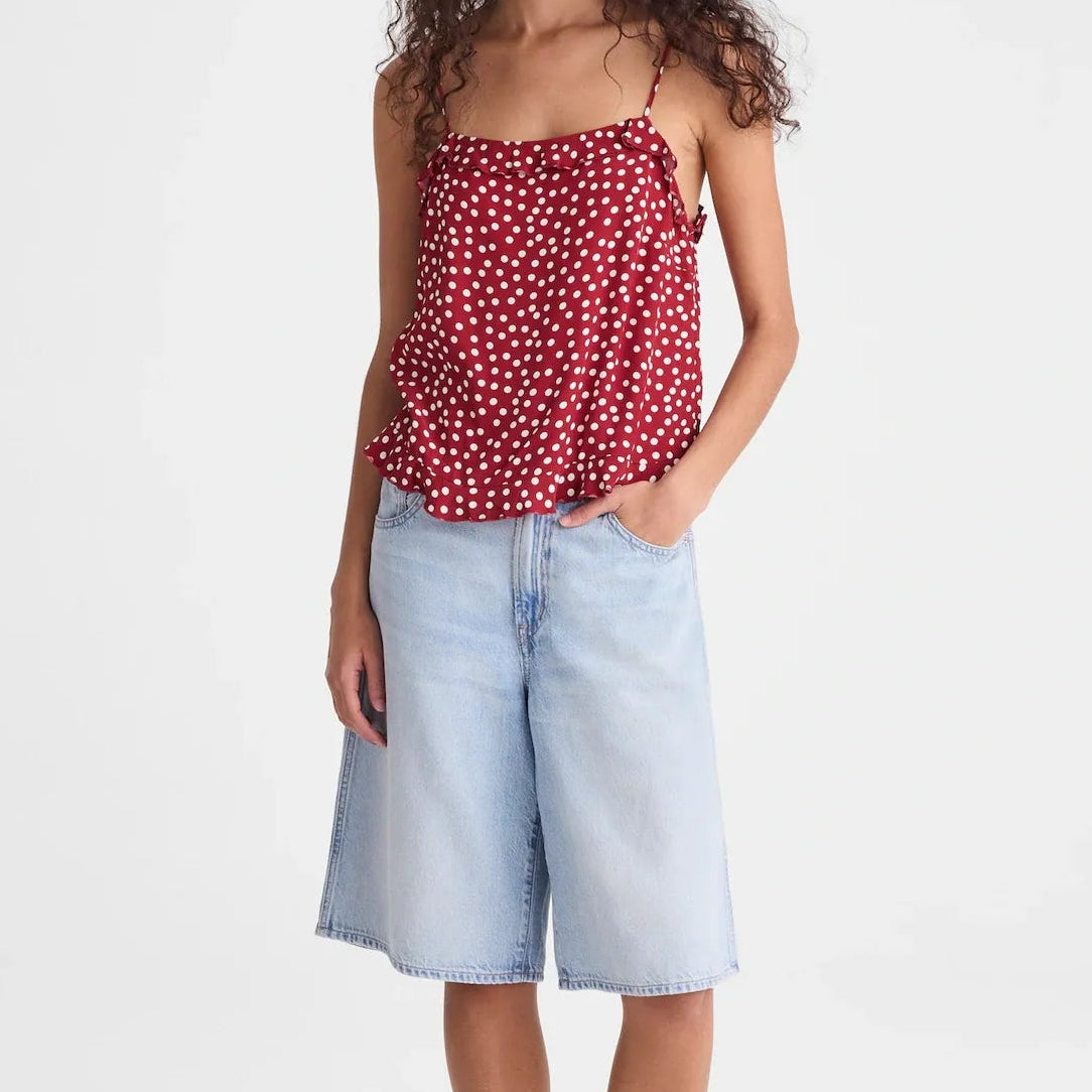 A woman modeling a red and white polka dot spaghetti strap top paired with light-wash denim culottes and brown sandals, standing against a plain white studio background.