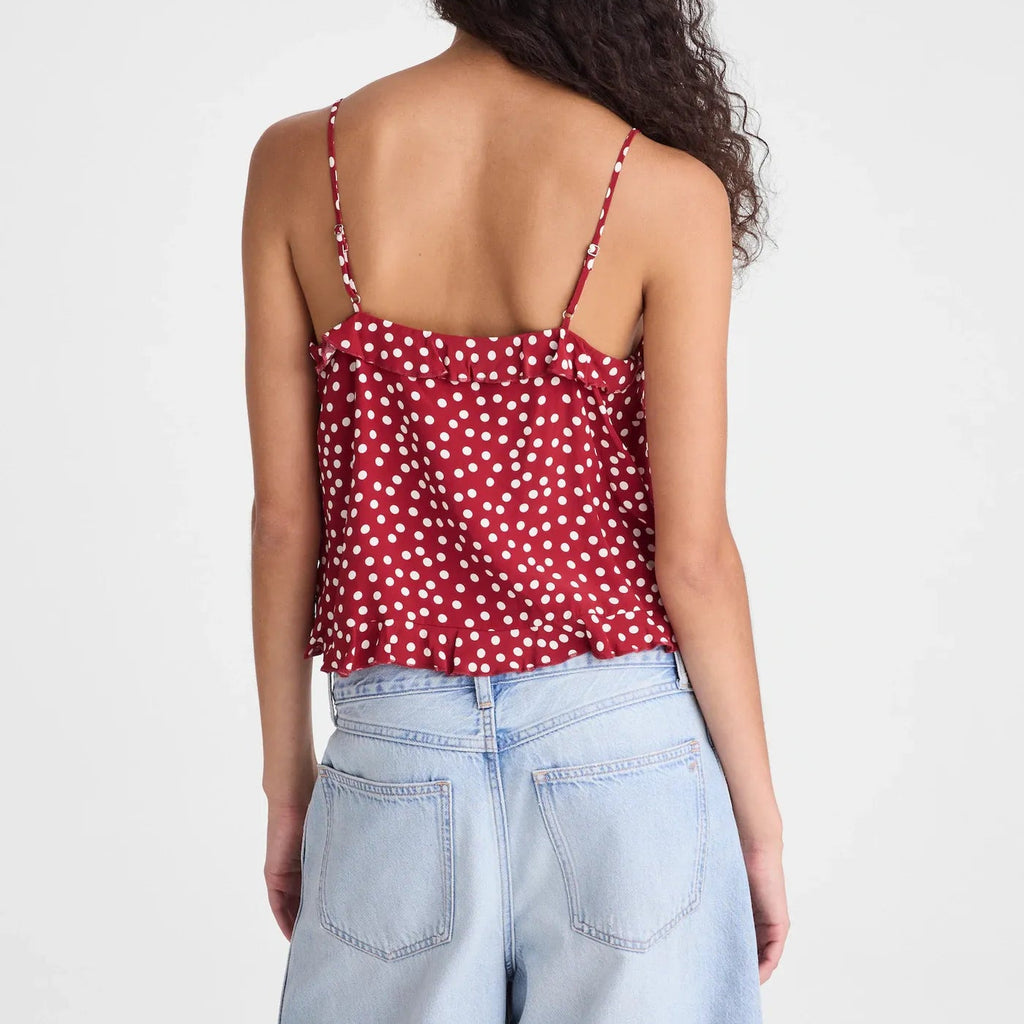 A woman shown from the back wearing a red spaghetti-strap top with a white polka dot pattern and light-wash blue jeans, set against a plain light gray studio background.