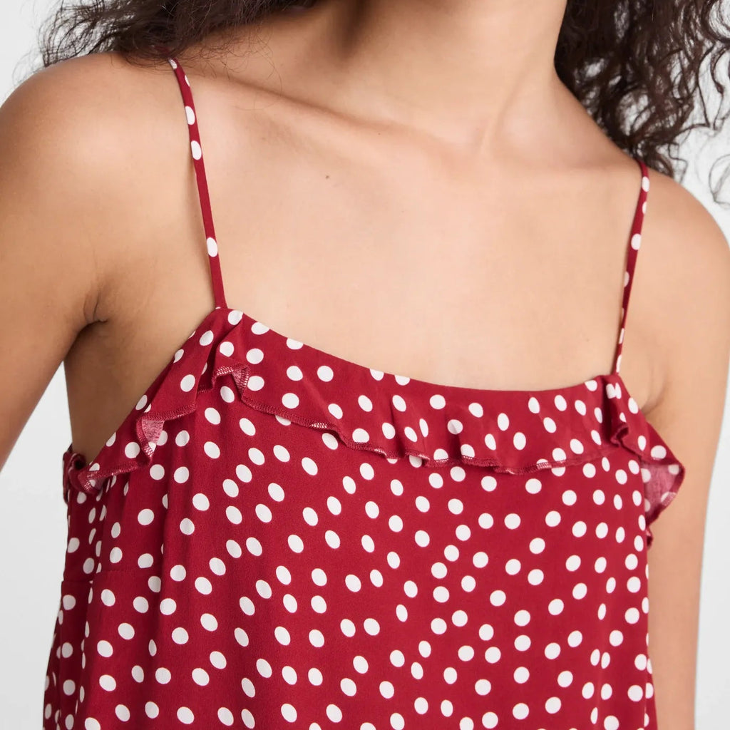 A close-up of a woman wearing a red camisole top with white polka dots and thin shoulder straps, against a plain light background.