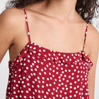 A close-up of a woman wearing a red camisole top with white polka dots and thin shoulder straps, against a plain light background.