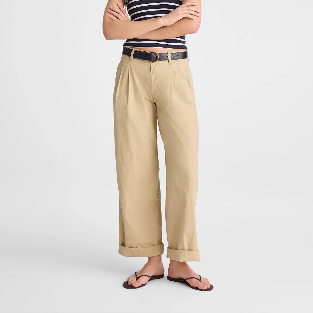 A woman modeling a navy and white striped strapless top, beige wide-leg cropped pants, a thin black belt, and dark brown sandals against a light gray studio background.