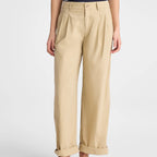 A person wearing beige wide-leg cropped trousers with a cuffed hem, paired with a navy and white striped top and dark brown flip-flop sandals, shown against a light gray studio background.