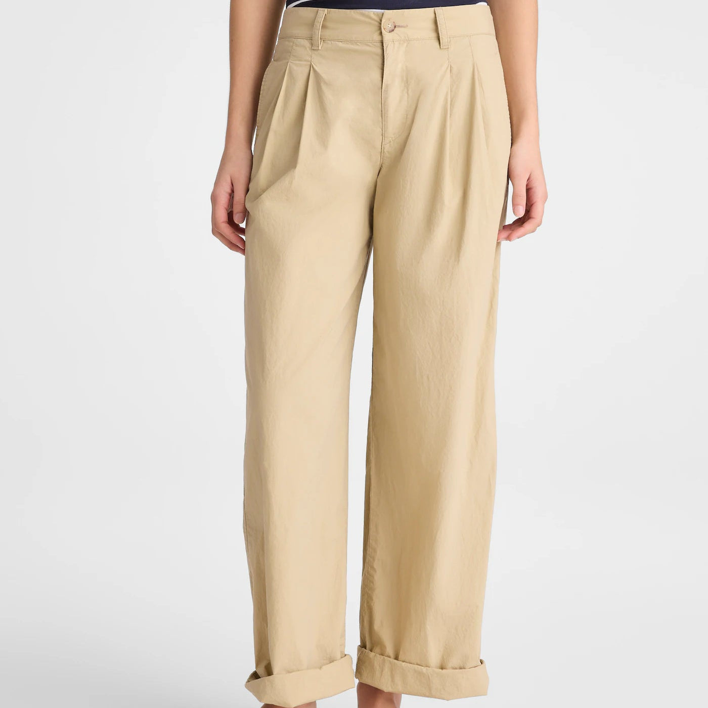 A person wearing beige wide-leg cropped trousers with a cuffed hem, paired with a navy and white striped top and dark brown flip-flop sandals, shown against a light gray studio background.