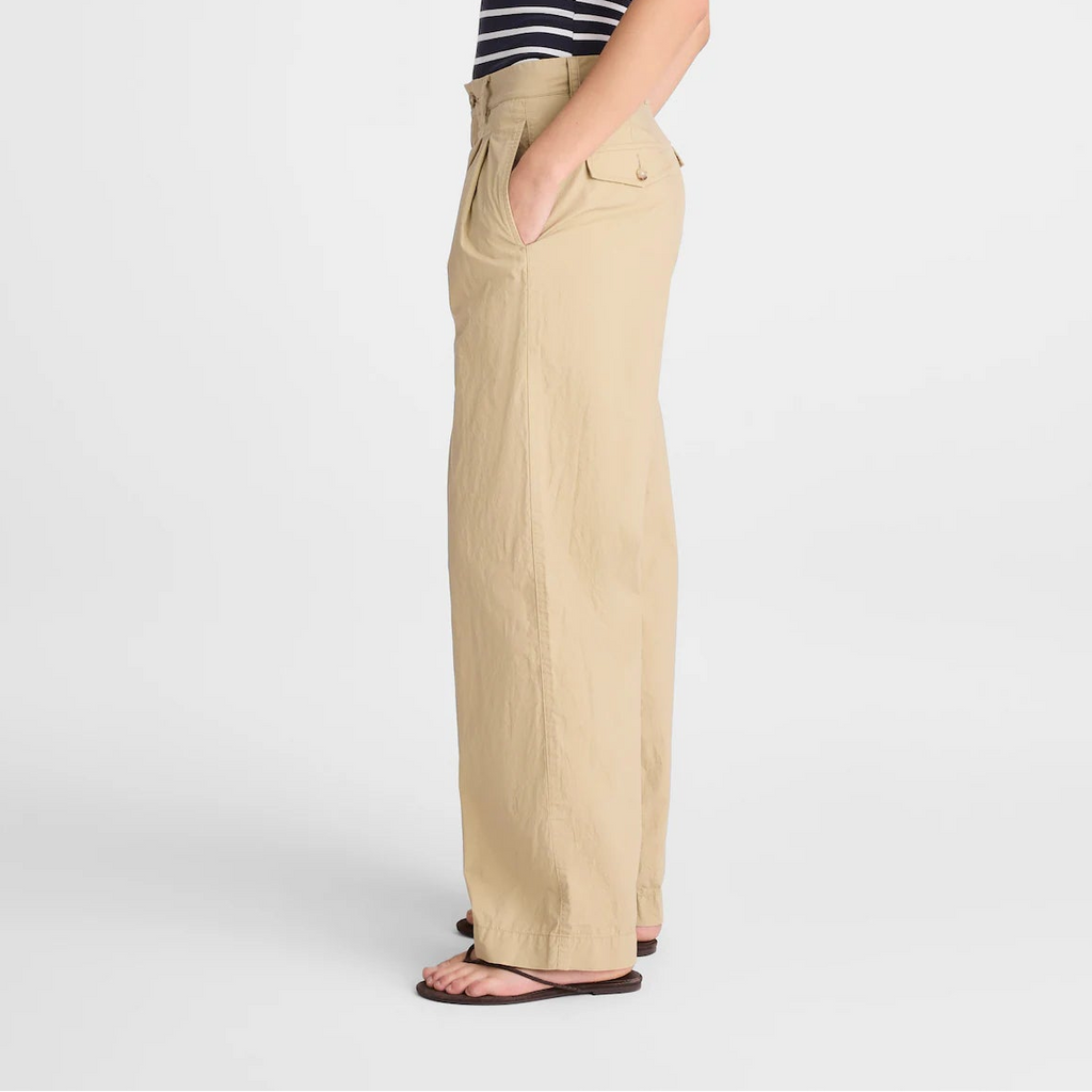 A woman stands in profile wearing a navy and white striped strapless top and beige wide-leg pants against a light gray studio background.