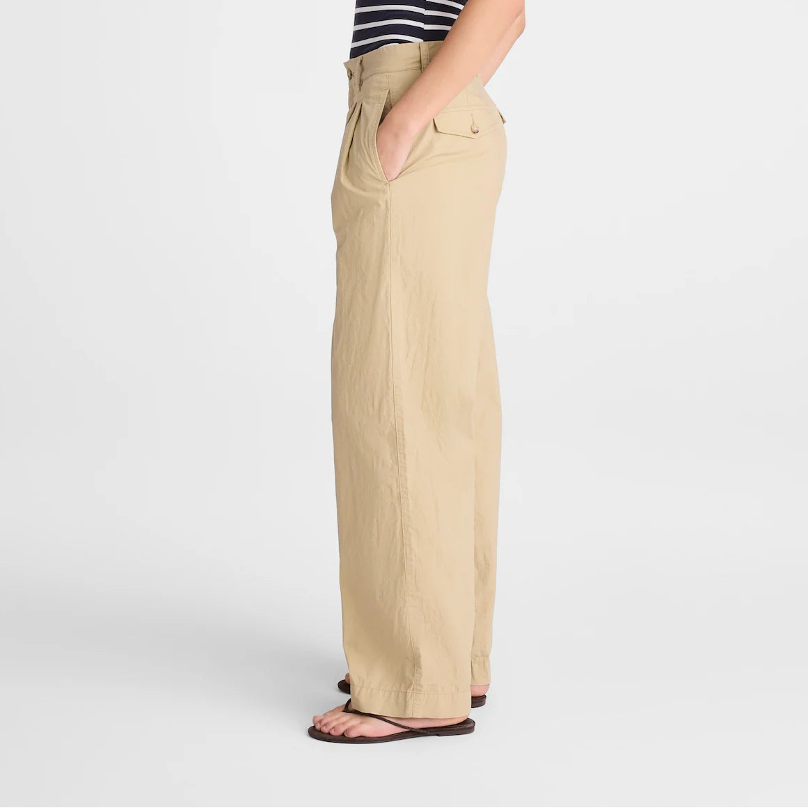 A woman stands in profile wearing a navy and white striped strapless top and beige wide-leg pants against a light gray studio background.