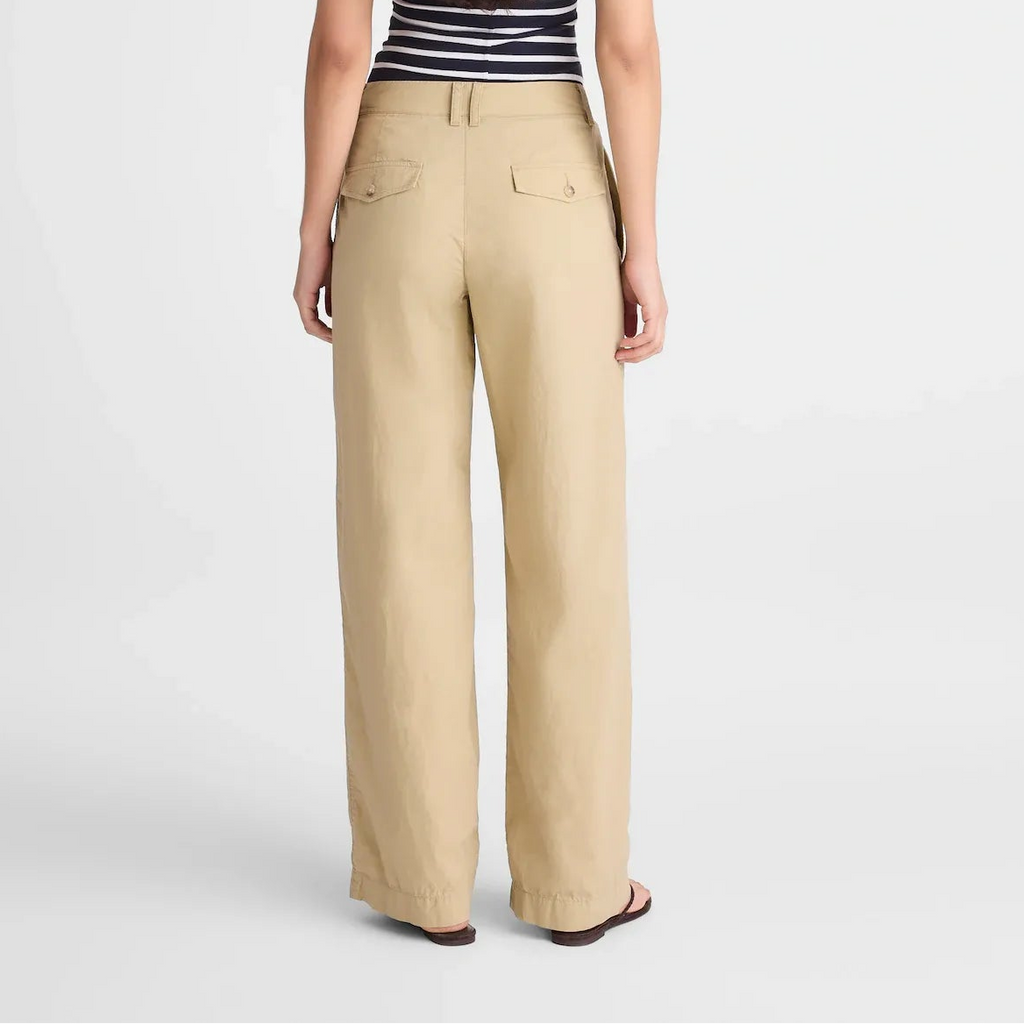 A woman viewed from the back wearing beige wide-leg trousers, a black and white striped tank top, and flat sandals against a light gray studio background.